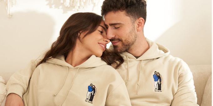 a couple sitting on a couch with matching embroidered hoodies