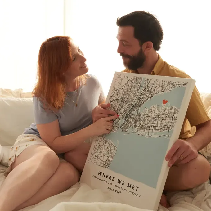a man and woman sitting on a bed looking at a map