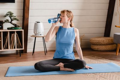 Woman sitting on a yoga mat drinking water from a blue glass bottle