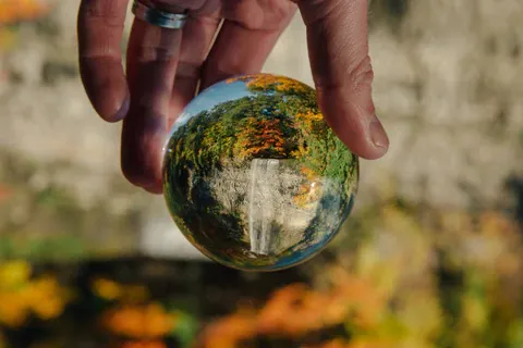 Hand holding lens ball with trees and waterfall
