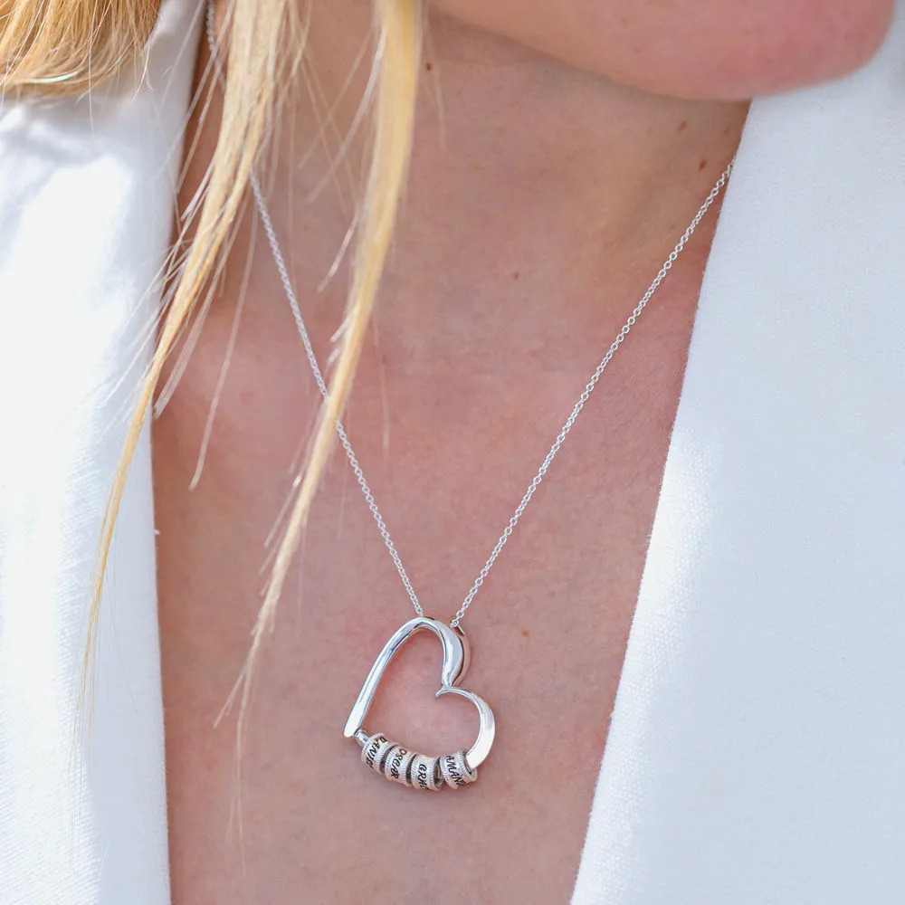 Close-up of a silver necklace with a heart-shaped pendant with inscribed beads around a woman's neck