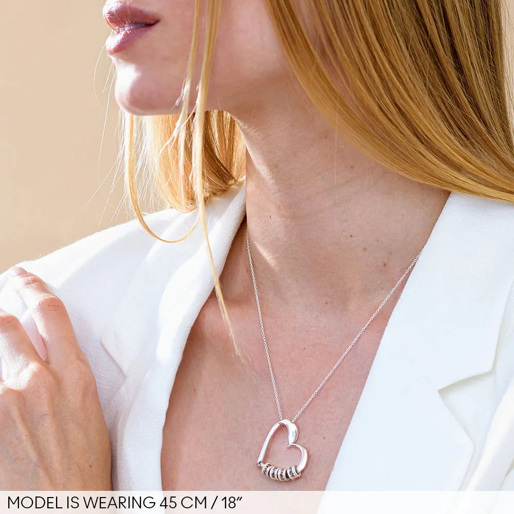 Woman wearing a silver necklace with a heart-shaped pendant with inscribed beads