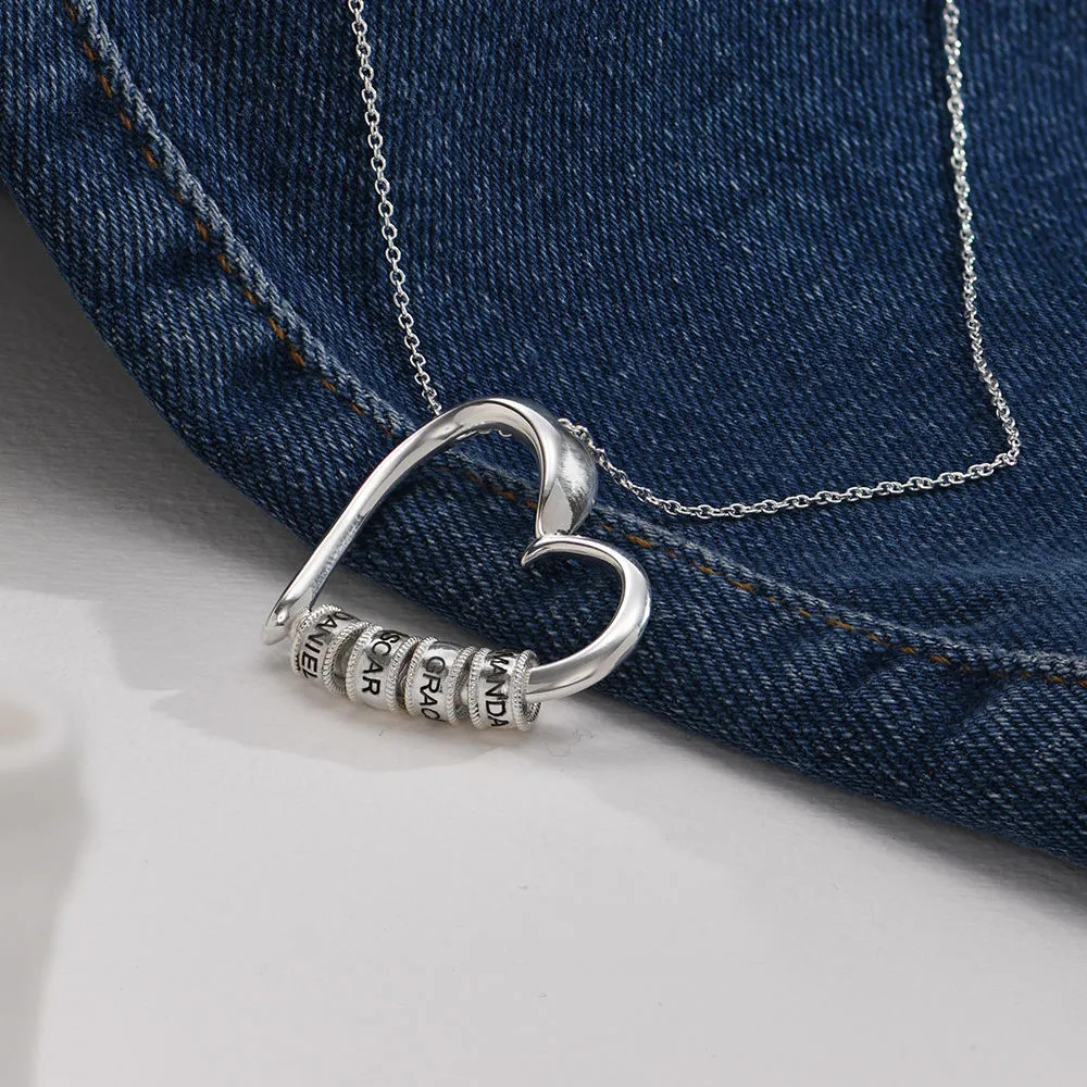 Silver heart-shaped necklace with engraved beads displayed over a jeans material