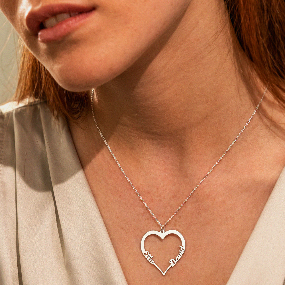 A woman wearing  a silver necklace with  a heart shaped pendant made from  names 