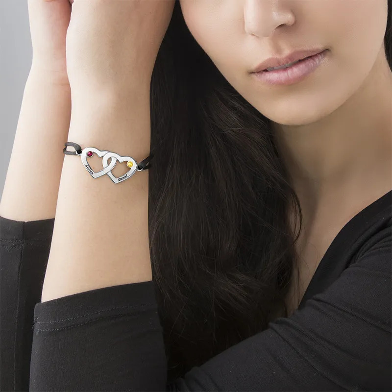 A woman wearing a couples bracelet with two interlocking hearts with borthstones 