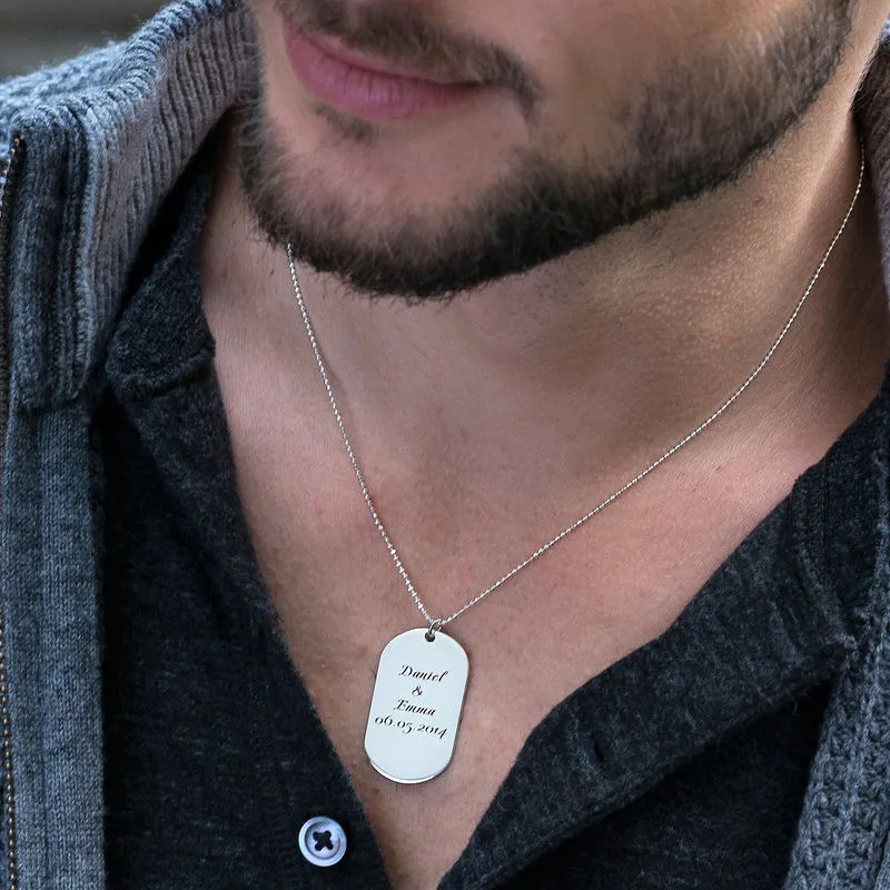 A man wearing a sterling silver necklace with an engraved dog tag pendant 