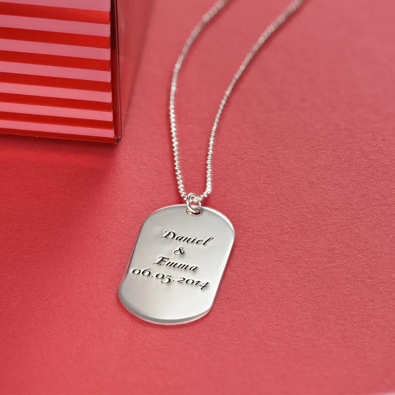A sterling silver necklace with an engraved dog tag pendant on a blush pink background 