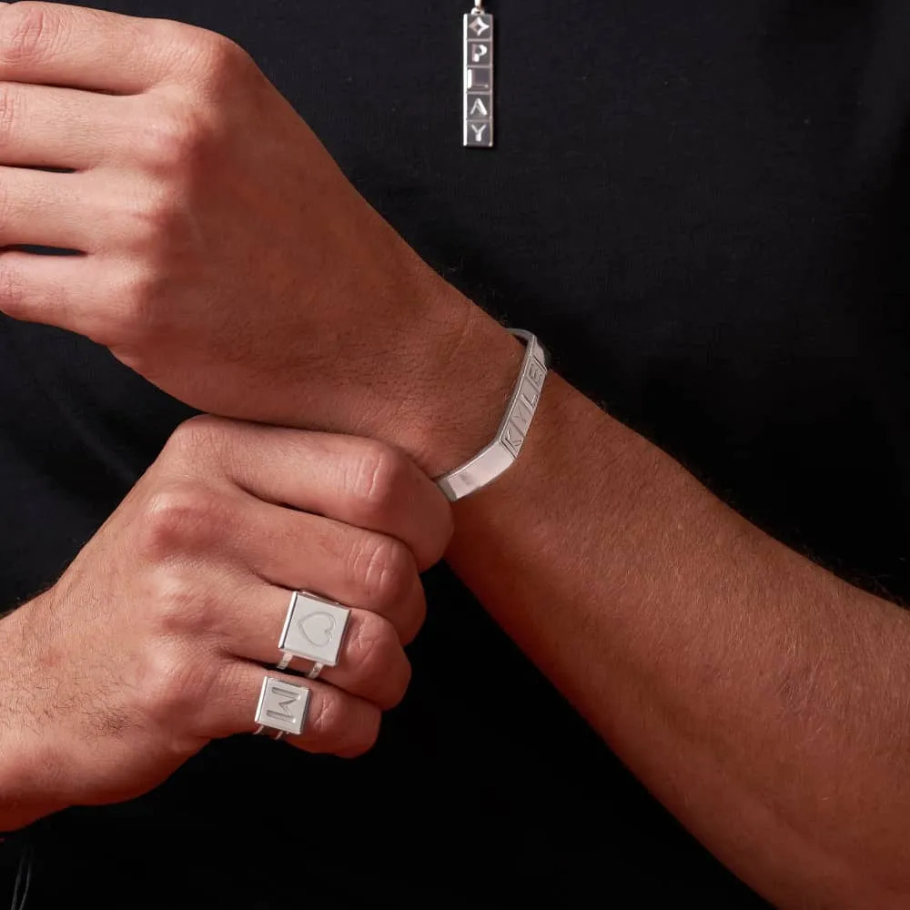 A man wearing a sterling silver wrist band with Domino tile initials while clasping his wrist 