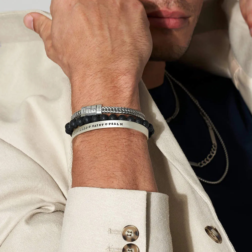 Man wearing a layered stainless steel bracelet with inscribed charms on their wrist