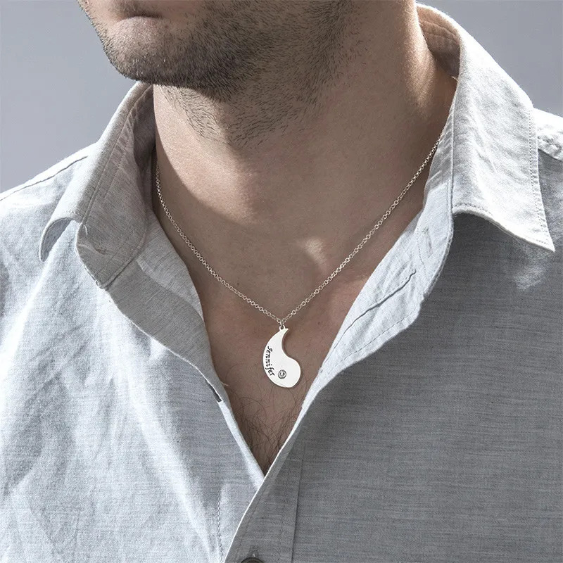 A man wearing one half of a yin yang couples necklace  with engraving and a birthstone 