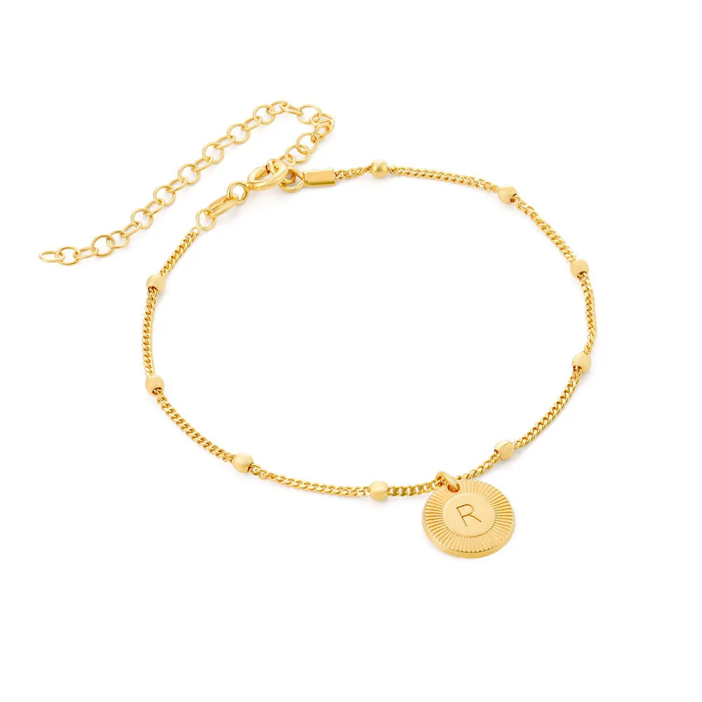 A gold bracelet with a circular charm engraved with an initial 