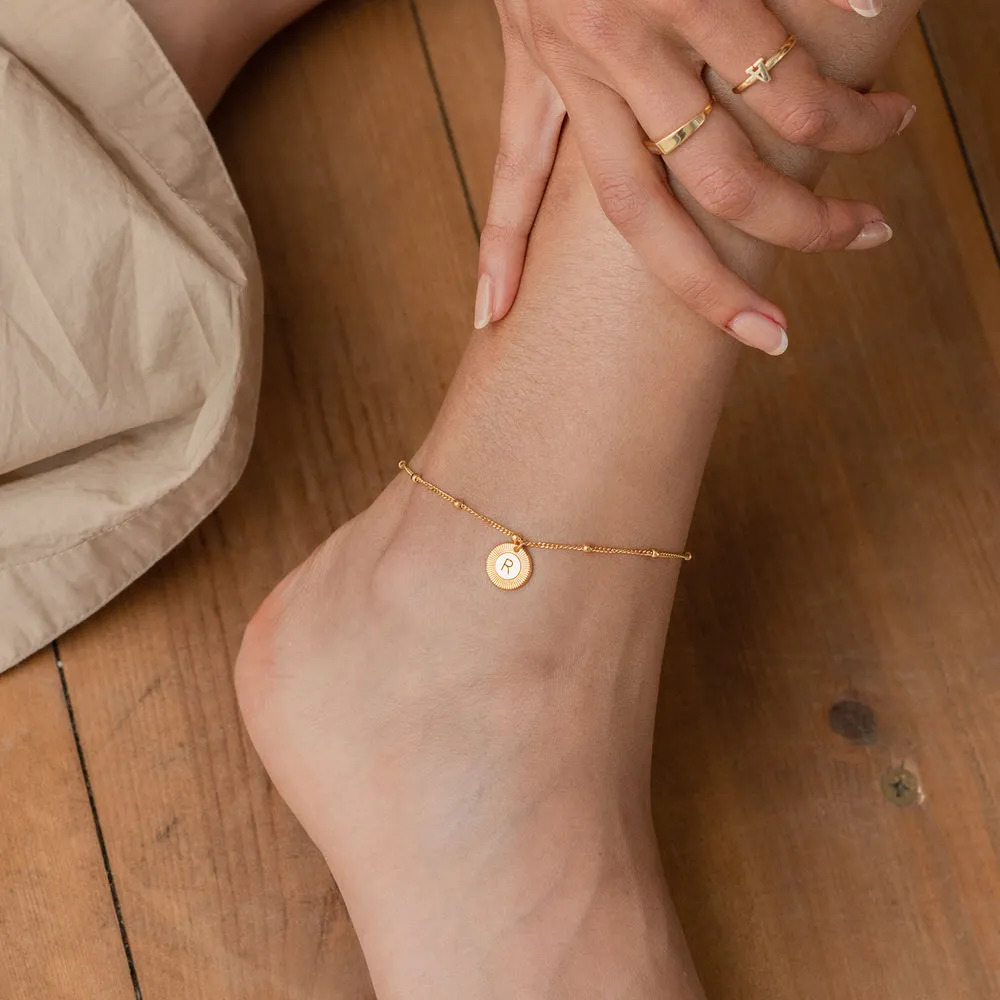 Woman wearing a gold anklet with an engraved  circular pendant