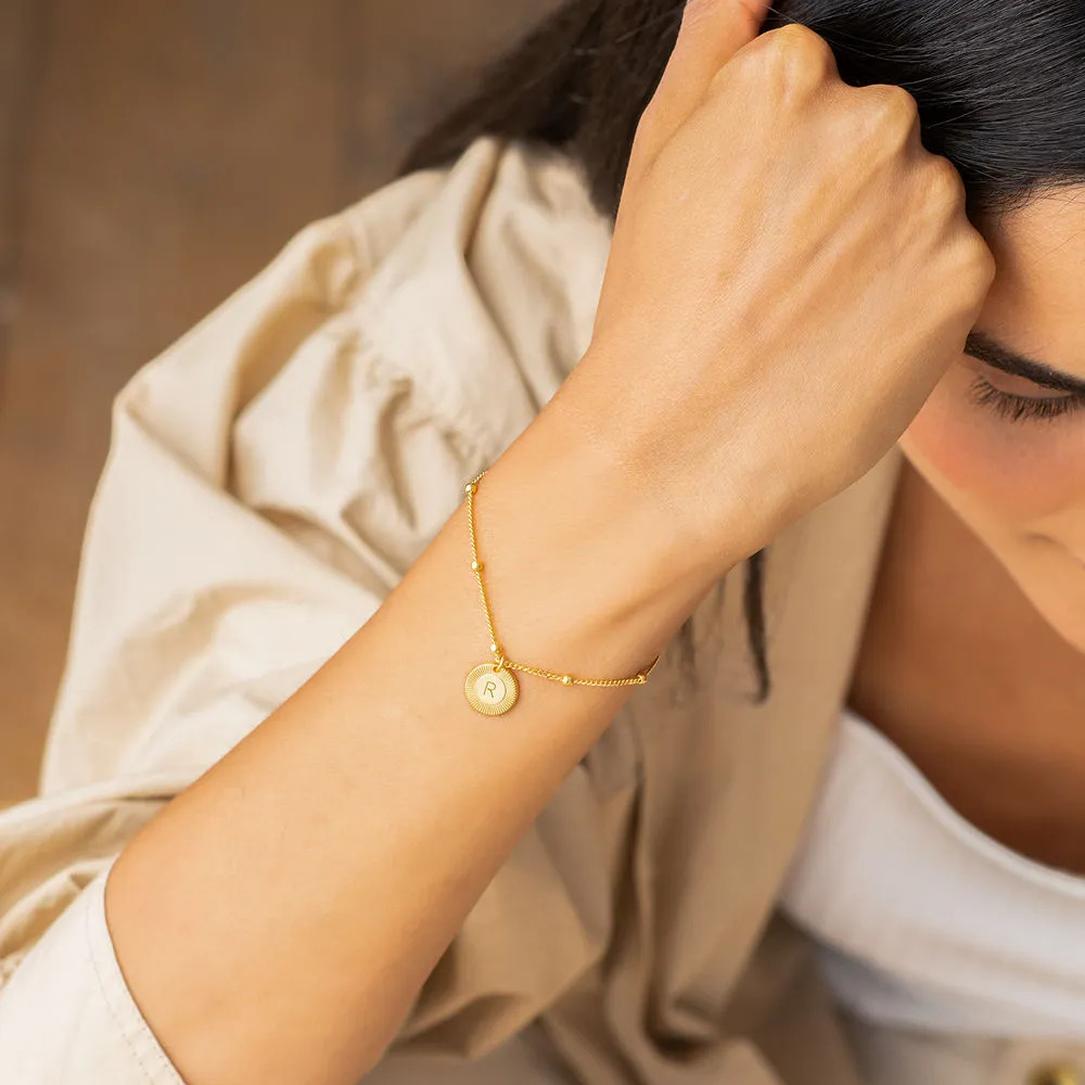 Woman wearing a gold bracelet with an engraved  circular pendant