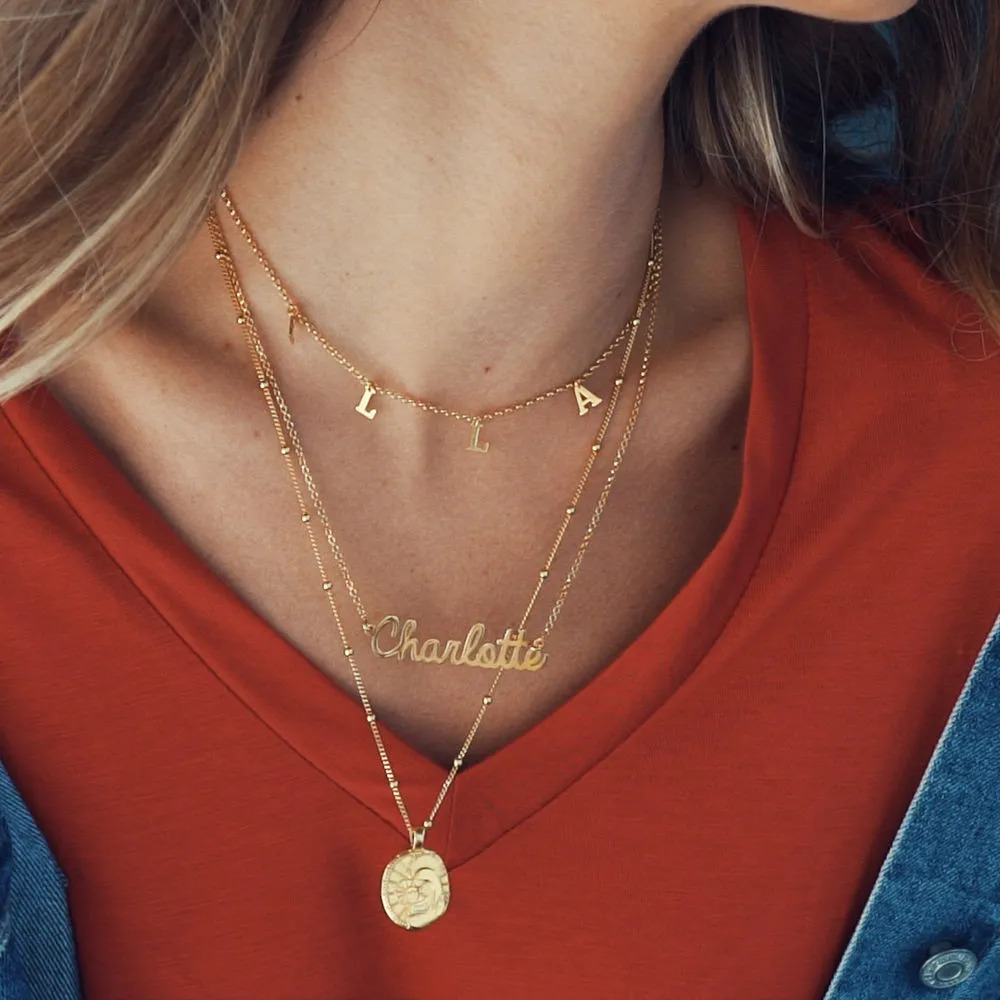 Woman wearing multiple gold necklaces with name pendants