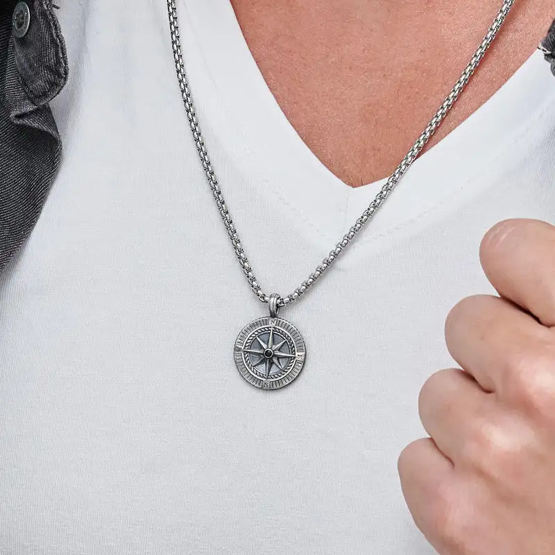 A silver necklace with a round pendant designed like a compass around a man's neck