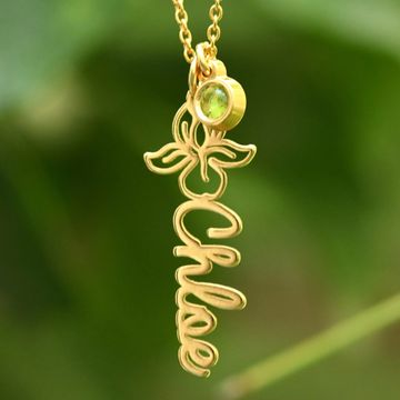 Close up of a gold name necklace with a green birthstone