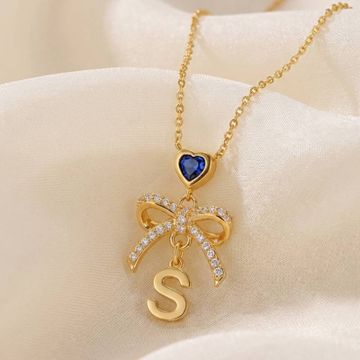 a gold S initial necklace with a blue heart and a bow