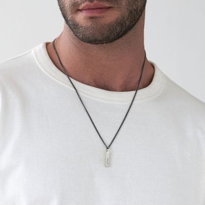 Man in a white shirt wearing a diagonal silver bar necklace inscribed with names