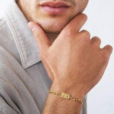 A man wearing a gold chain bracelet with a plate inscribed with "1981"