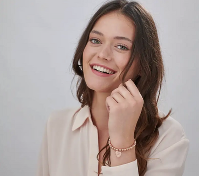 Woman smiling and wearing an inscribed charm bracelet in rose gold plating
