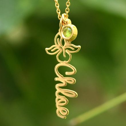 Close up of a gold name necklace with a green birthstone
