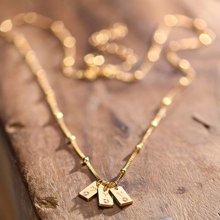 a close up of a gold necklace with pink birthstones on a wooden surface