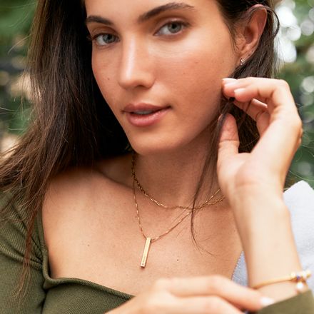 a woman in a green shirt wearing a gold necklace with a pink birthstone