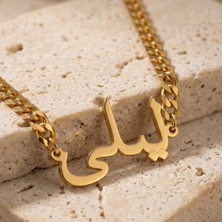 a close up of a Lilly Arabic gold name necklace on a brick