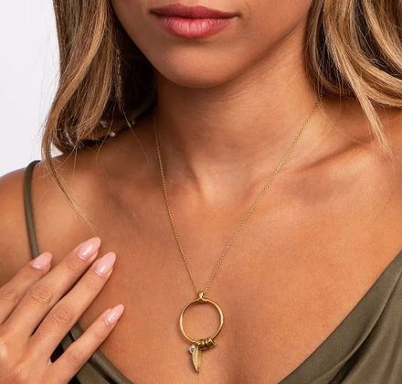 Woman wearing a gold necklace with a circle pendant with engraved beads and a feather detail