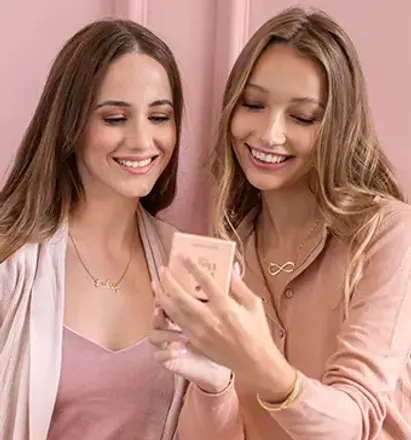 two beautiful women standing next to each other looking at a cell phone