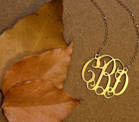 MYKA's Celebrity Monogram Necklace in gold next to decorative autumn leaves