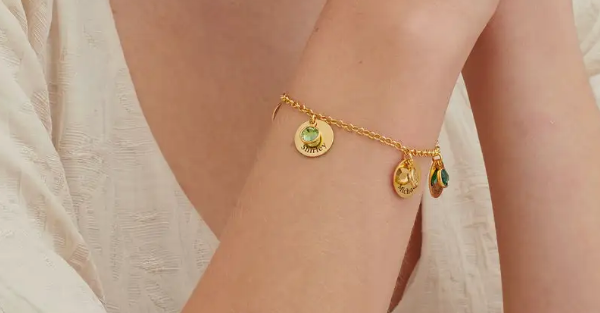 A gold bracelet with round inscribed charms with birthstone crystals around a woman's wrist