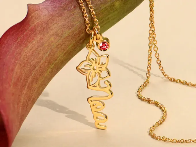 a gold necklace with a flower and a name on it