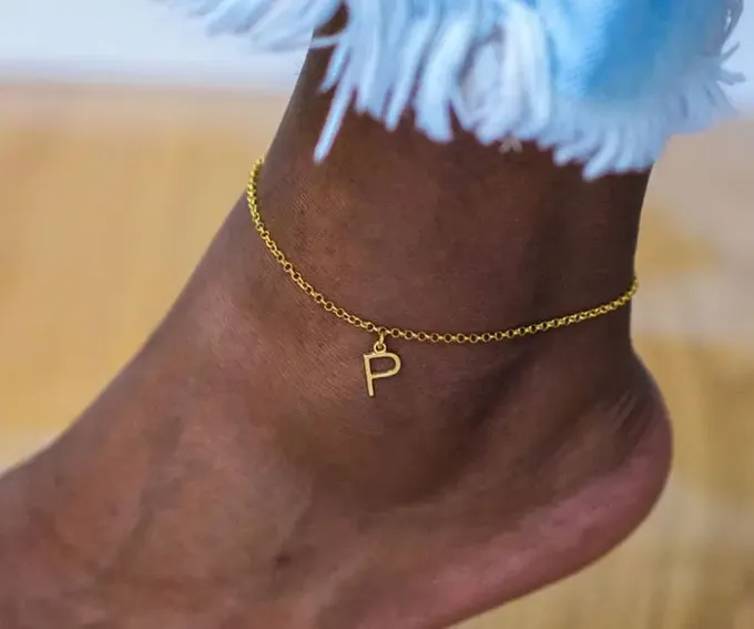 a close up of a person's foot wearing a gold ankle chain