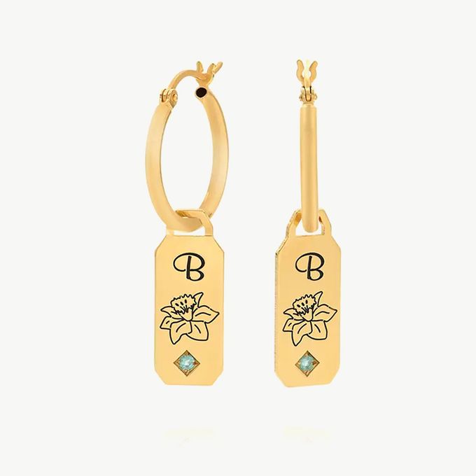 a pair of gold earrings with a flower and initial