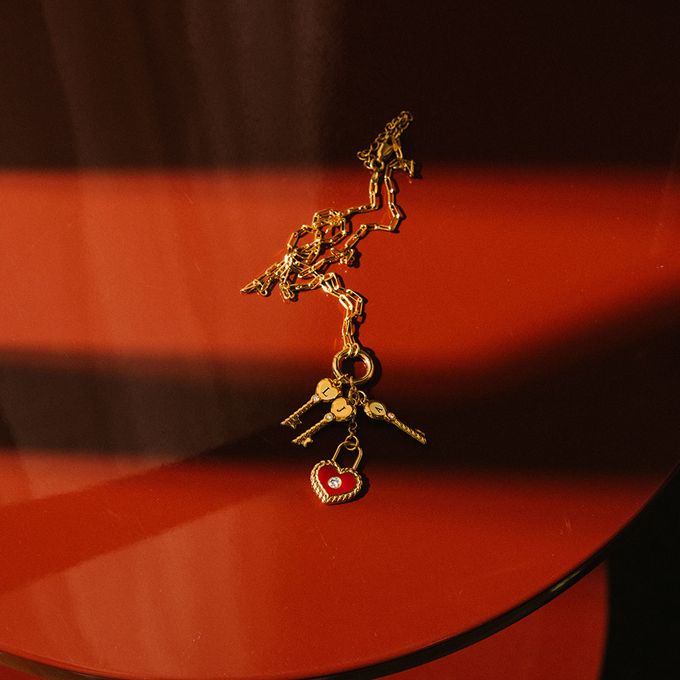 a close up of a gold with keys and a red heart padlocknecklace on a red table