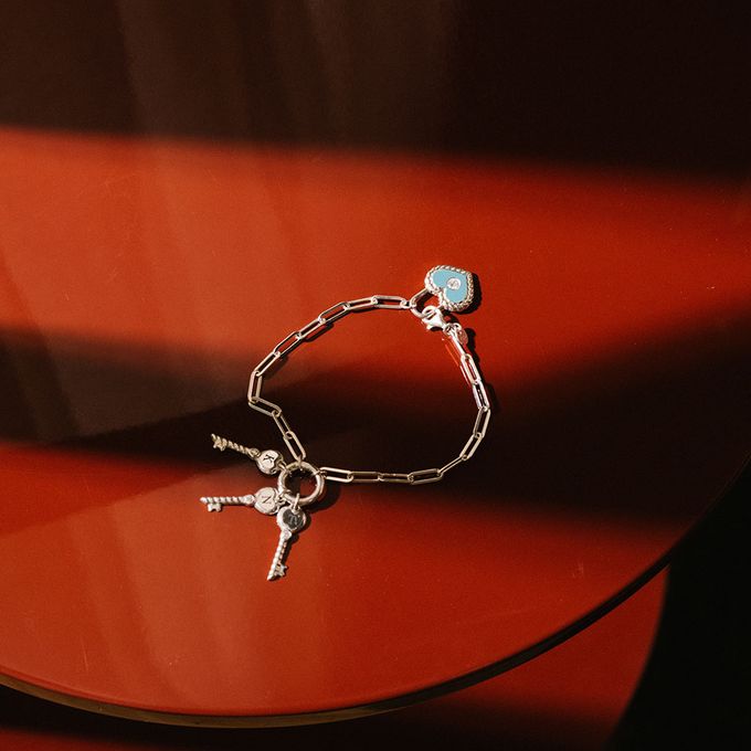 A red table with a silver bracelet with a keys and light blue pardlock