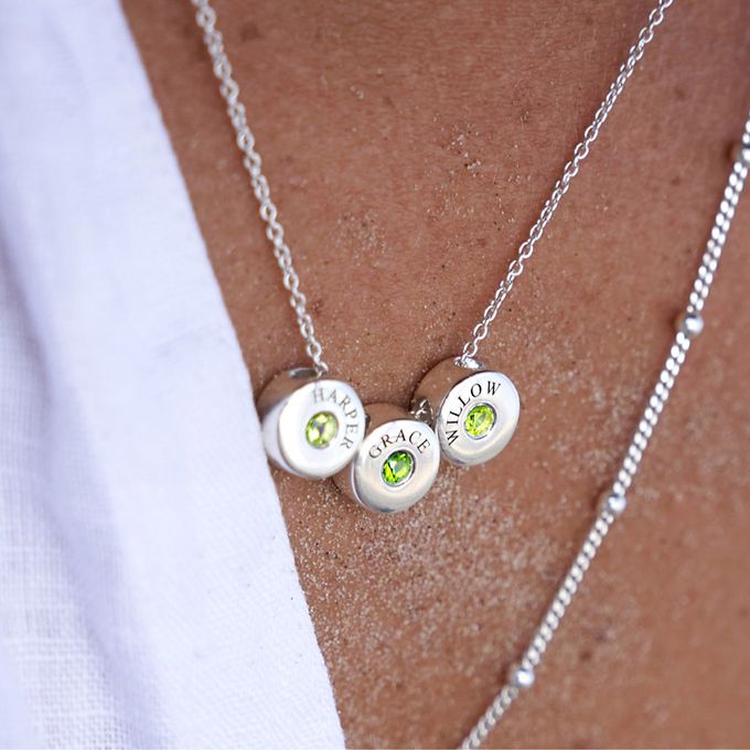 a close up of a person wearing a silver necklace with a green birthstone