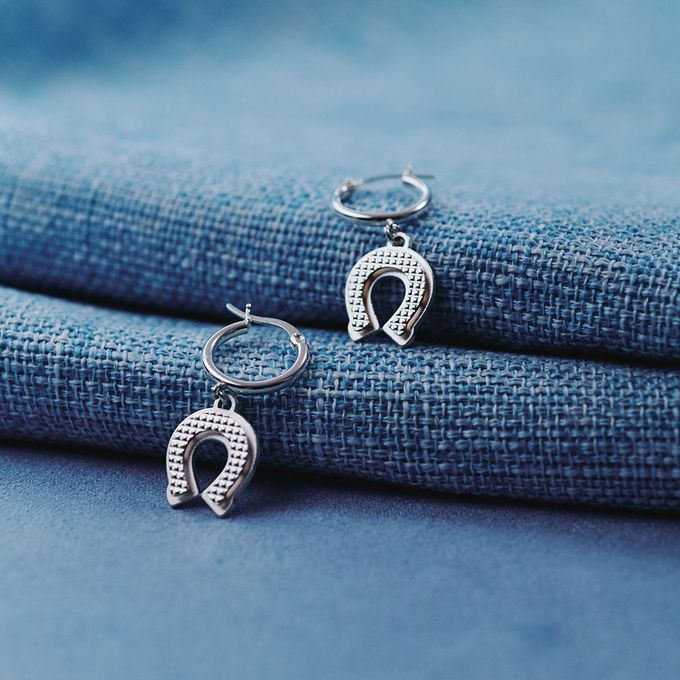 A pair of silver horseshoe earrings sitting on top of a blue cloth