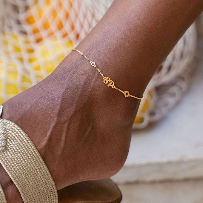a close up of a person's foot wearing a gold ruby anklet