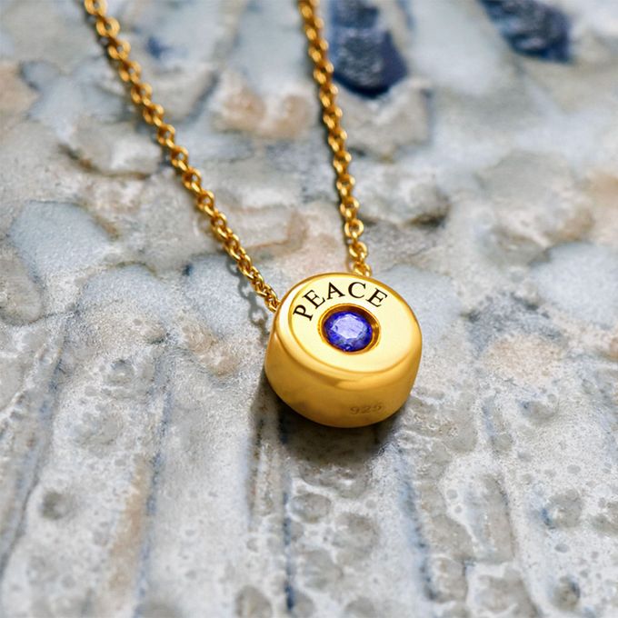 a gold name necklace with a blue stone in the center