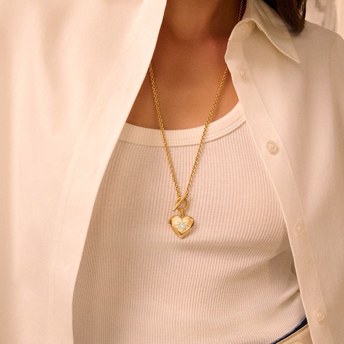 a woman wearing a white shirt and a gold heart locket necklace