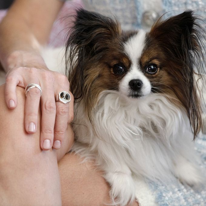 a woman holding a small dog on her lap wearing a ring with the dogs face on
