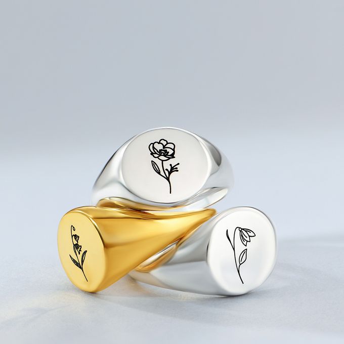 Gold and silver signet rings sitting on a grey surface