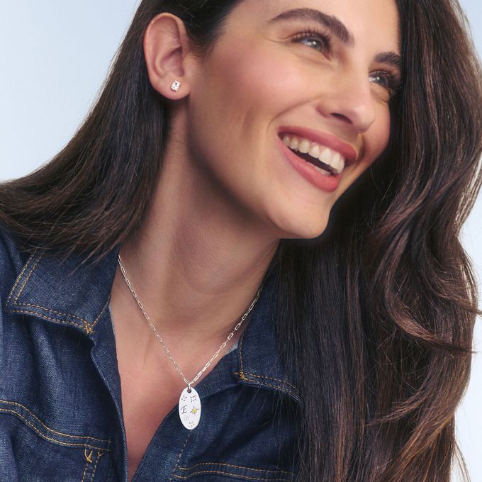 A woman wearing a silver birthstone necklace with the intial E on