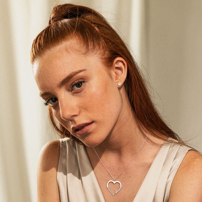 A woman wearing a silver necklace with a heart shaped pendant made from names