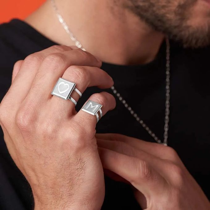 A man wearing Domino tile shaped initial rings on his pinky and ring finger