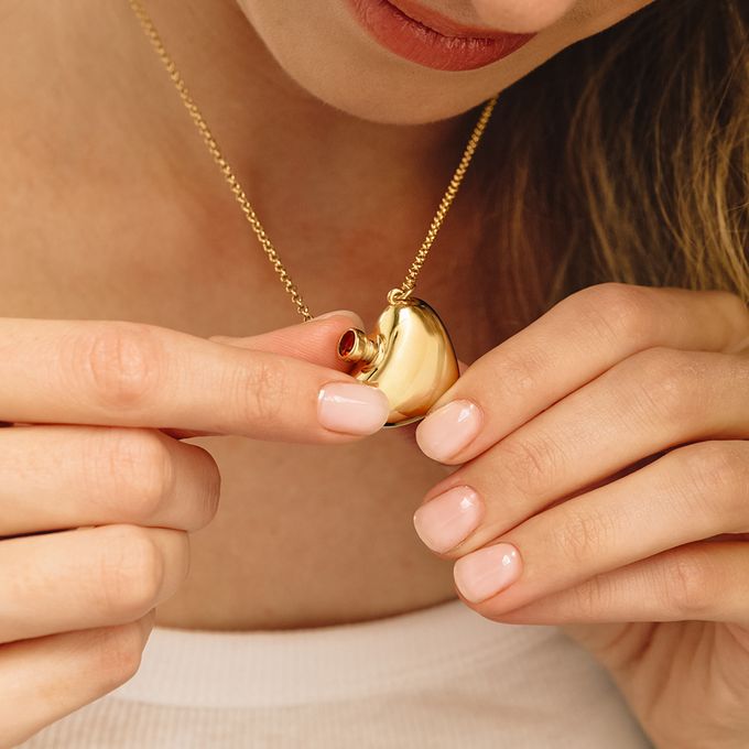 a woman is holding a gold necklace with a heart on it