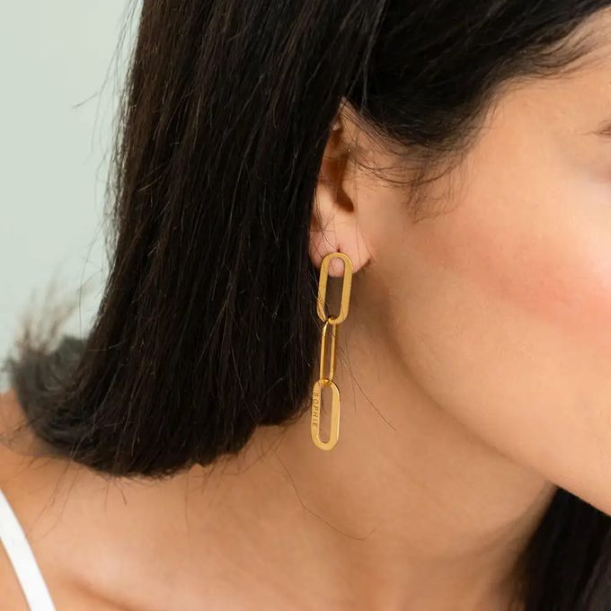 Woman wearing gold chain link earrings with three links inscribed with "Sophie"