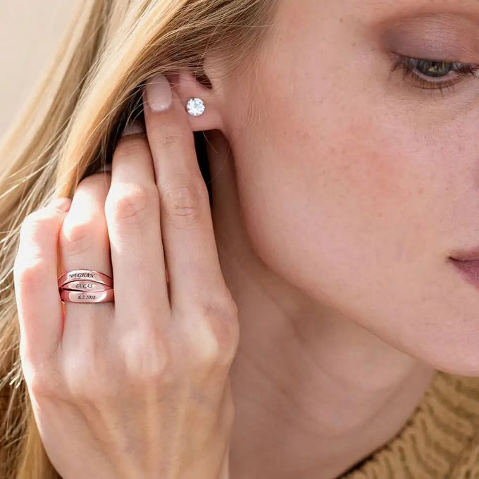 Woman touching her ear with a diamond earring wearing a rose gold interlocking engraved ring on her finger